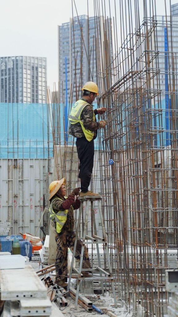 Two construction workers on site erecting steel framework for urban skyscrapers.